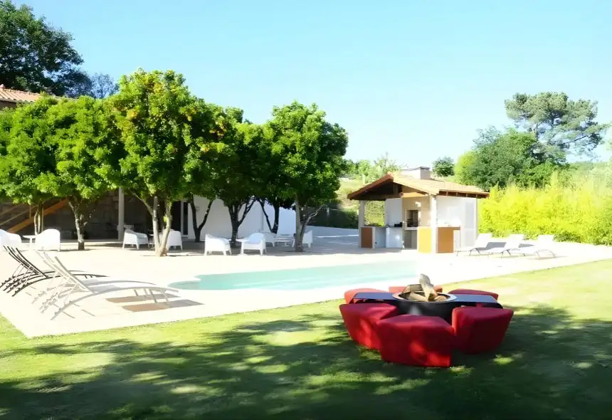 Outdoor bioethanol fireplace pit by GlammFire, surrounded by circular red cushioned seating in a landscaped leisure area with pool and cabana.